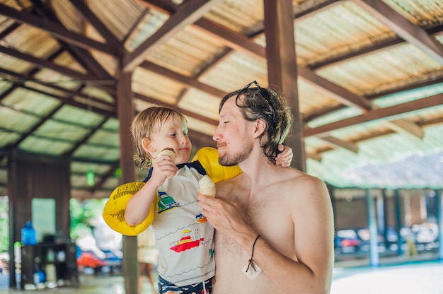 Pai e filho tomando sorvete no parque aquático sob um telhado de colmo