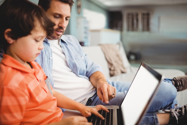 Pai e filho trabalhando no laptop enquanto está sentado no sofá