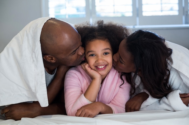 Pai e mãe beijando sua filha na cama