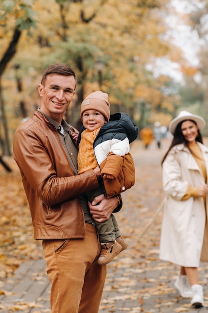 Pai e mãe com filho caminhando no parque outono. Uma família caminha no outono dourado em um parque natural.