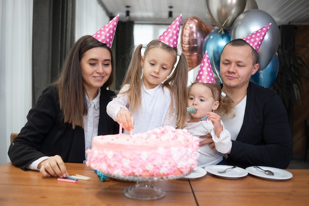 Pai e mãe de meninas de férias para crianças na mesa com um bolo. ele pousa as velas.