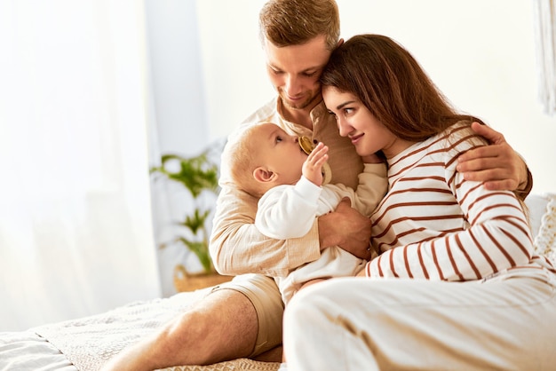 Pai e mãe estão sentados na cama segurando o bebê nos braços e rindo dele felicidade da família copiar espaço