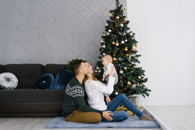 Pai e mãe seguram seu filho perto de uma árvore de natal