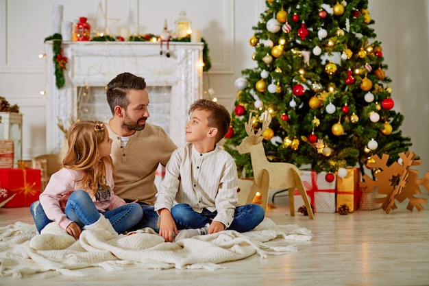 Pai e seus dois filhinhos, sentado junto à chaminé da lareira na véspera de natal