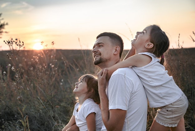 Pai e suas filhas no campo ao pôr do sol.