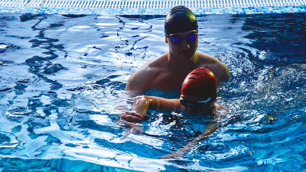 Pai e treinador ensinam o filho a nadar, se divertem, brincam e mergulham em uma piscina azul