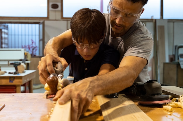 Pai ensinando carpintaria ao filho e lixando madeira.