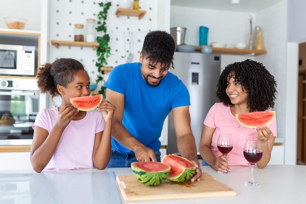 Pai está cortando melancia enquanto mãe e filha o observam