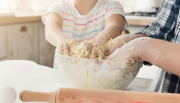 Pai está cozinhando massa com a filha na cozinha. Homem e menina com as mãos amassando a massa na tigela, close-up, copie o espaço