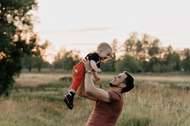 Pai feliz brinca com o filho sorridente no campo de verão ao pôr do sol