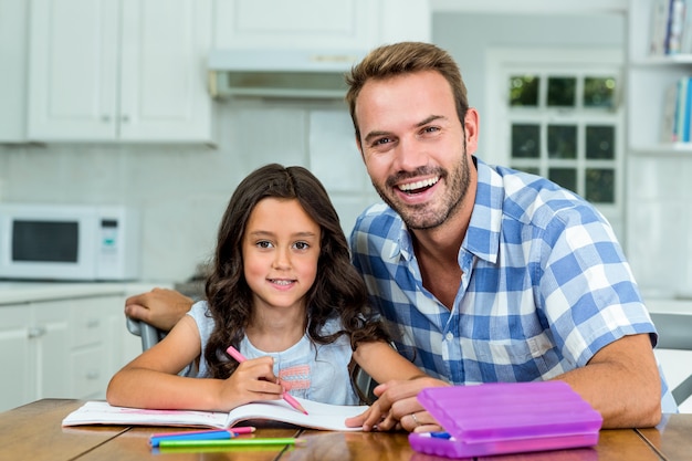 Pai feliz com a filha escrevendo no livro na mesa