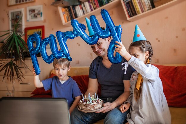 Pai feliz com dois irmãos comemorando aniversário via internet em tempo de quarentena, auto-isolamento