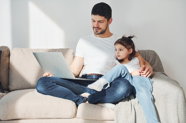 Pai feliz com sua filha passando tempo livre com laptop em casa juntos