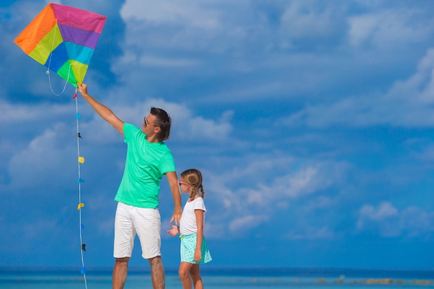 Pai feliz e fofa filha empinando pipa juntos na praia tropical