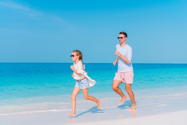 Pai feliz e sua adorável filha na praia de areia branca se divertindo