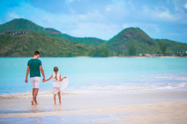 Pai feliz e sua adorável filha pequena na praia tropical caminhando juntos