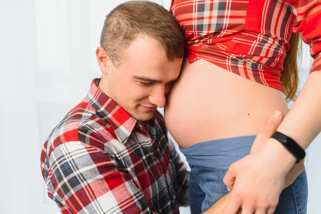 Pai feliz ouvindo a barriga grávida da mãe fechar os olhos.