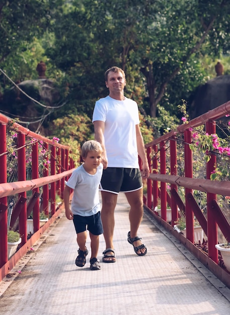 Pai Filho caminhar passar tempo juntos explorar novo Olhar para a câmera Atravessar ponte suspensa de ferro vermelho caminho floresta Criança segurar puxar Mão do homem Levantar menino dia dos pais união familiar influência futura criança viver