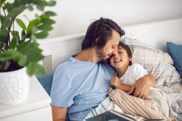 Pai lê um livro deitado em uma cama branca para seu filho antes de ir para a cama