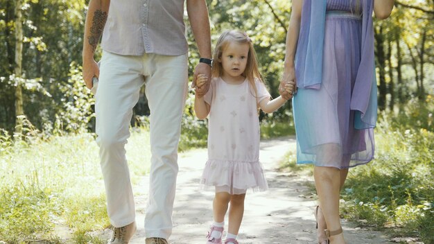Pai, mãe e filha caminhando no parque em um dia ensolarado, telefoto