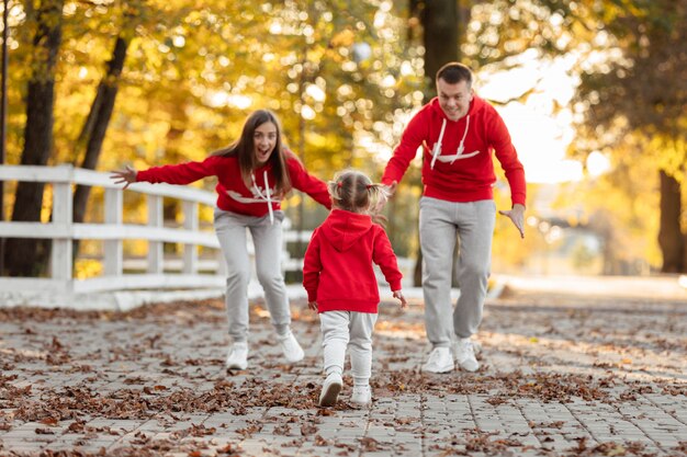 Pai, mãe e filha estão caminhando no parque outono, família feliz se divertindo ao ar livre.