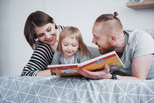 Pai, mãe e filha lendo o livro infantil em um sofá na sala de estar. família grande e feliz ler um livro interessante em um dia festivo. os pais amam seus filhos