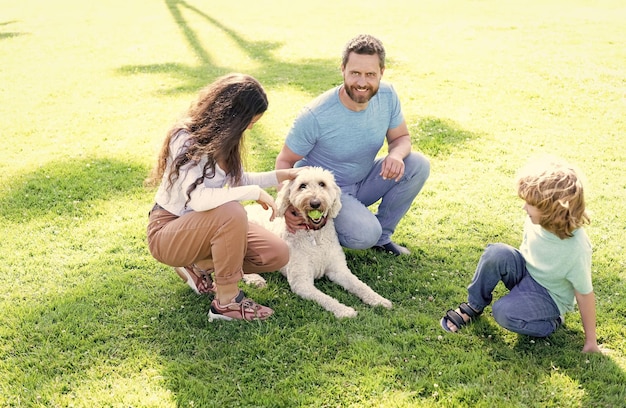 Pai mãe e filho na família amigável da grama do parque verde com animal de estimação