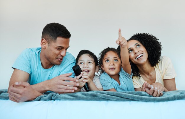 Pai mãe e filhos na cama assistindo tv e sorrindo para um filme engraçado de comédia ou apontando para a casa da família Pais felizes filhos e assistem a programas de televisão com assinatura de streaming ou riem juntos