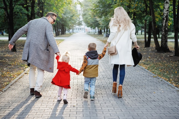 Pai, mãe, filho e filha da família estão correndo ao longo de uma rua pavimentada em um parque.