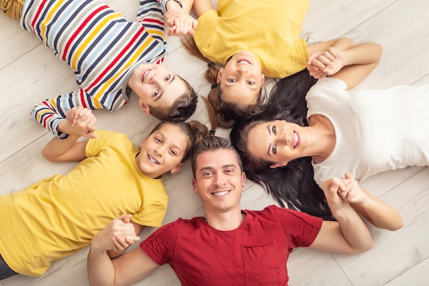 Pai, mãe, meninas gêmeas e um menino estão deitados no chão de mãos dadas e sorrindo.