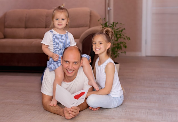 Pai mantém um cartão de filhas alegres no dia dos pais durante as férias em casa