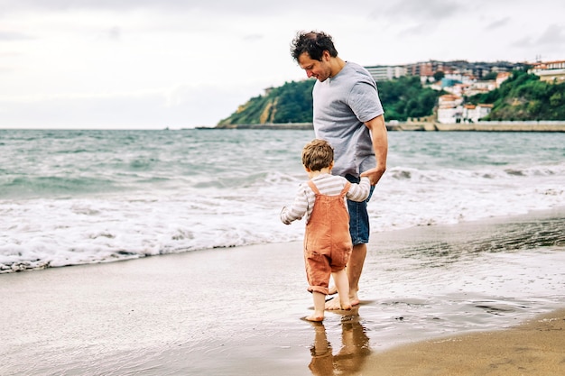Foto pai milenar com seu filho de três anos brincando com o olá na praia