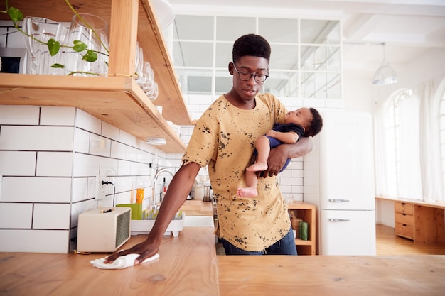 Pai multitarefa segura filho adormecido e limpa a cozinha