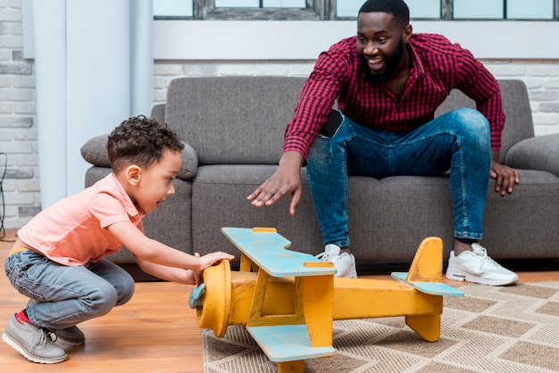 Pai negro e filho brincando com o avião grande brinquedo