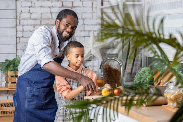 Pai negro e seu filho cozinhando legumes frescos na cozinha em casa Pai africano e menino preparando juntos