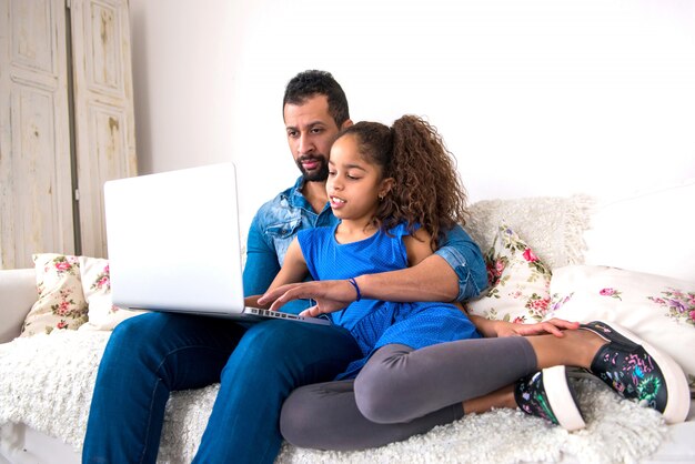 Pai negro e sua filha em um sofá com um laptop