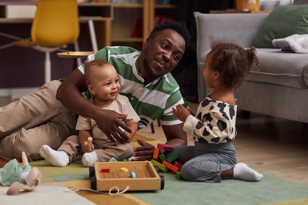 Pai negro feliz com dois filhos em casa brincando com brinquedos juntos