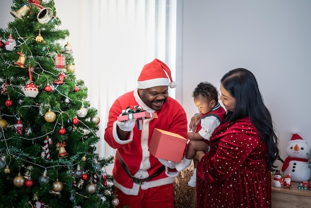 Pai nigeriano de família africana vestindo uma caixa de presente aberta de fantasia de Papai Noel vermelho para um filho de 4 meses