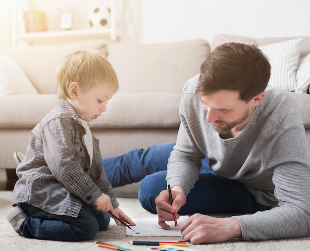 Pai passando um tempo e desenhando junto com seu filho pequeno, deitado no chão em casa