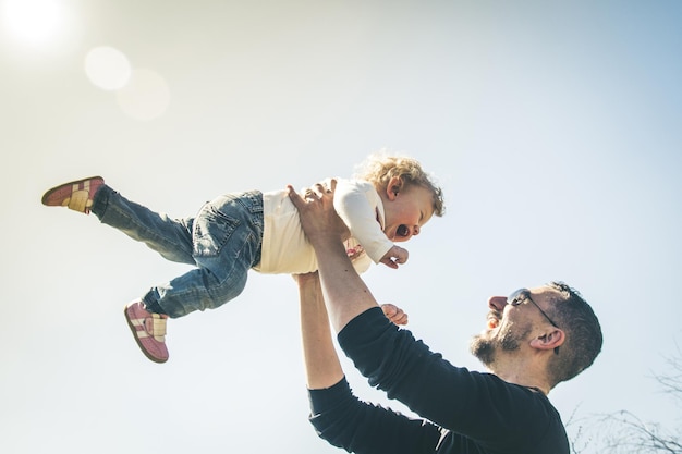 Pai pegando a filha enquanto está de pé contra o céu