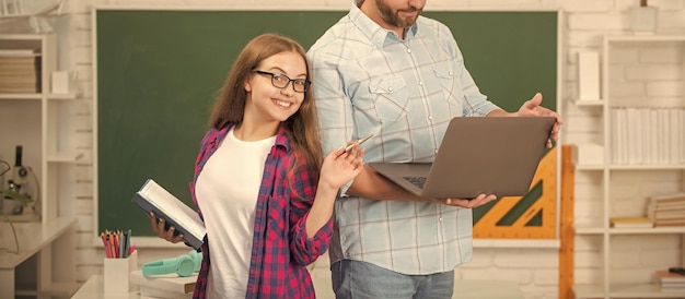 Pai recortado e criança feliz estudam na escola com livro e laptop na escola de fundo de quadro-negro