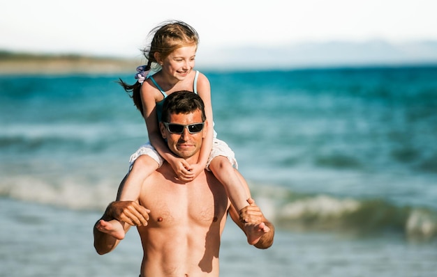 Pai segurando a filha nos ombros em retratos da costa do mar Pai de família e criança bonita na praia no verão juntos