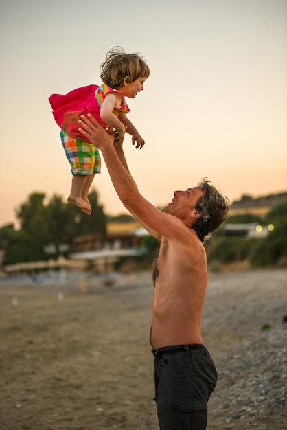 Pai sem camisa carregando filha enquanto está de pé na praia contra o céu
