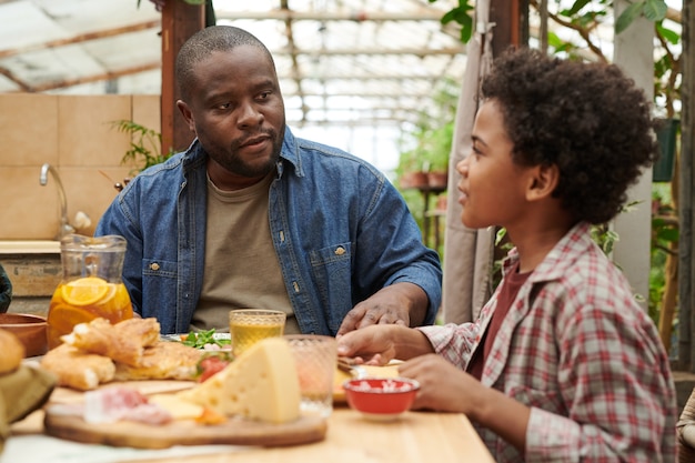 Pai sentado à mesa de jantar junto com seu filho conversando e jantando