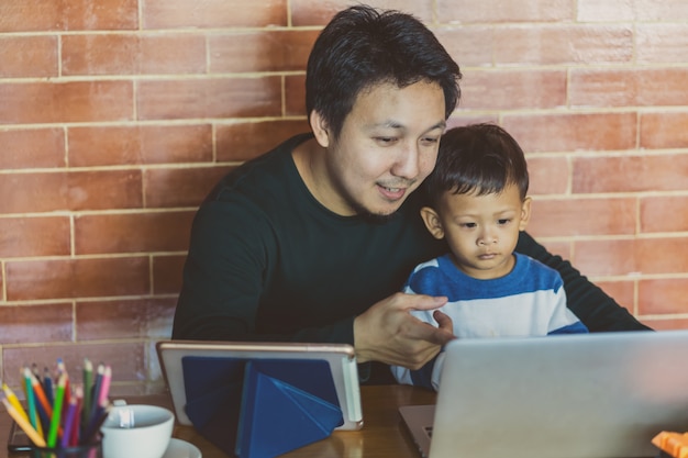 Pai solteira asiática com filho está olhando os desenhos animados via laptop de tecnologia juntos