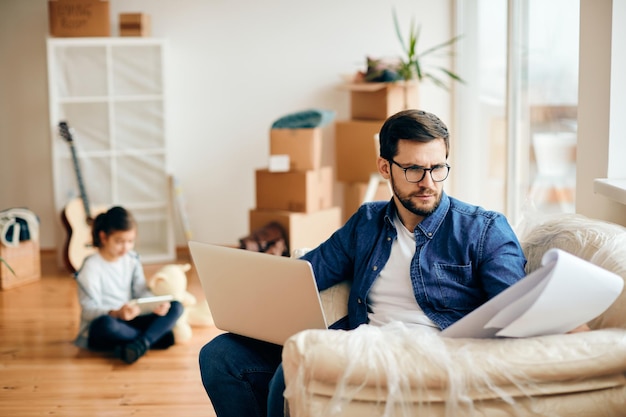 Pai solteiro analisando a papelada e usando laptop no novo apartamento