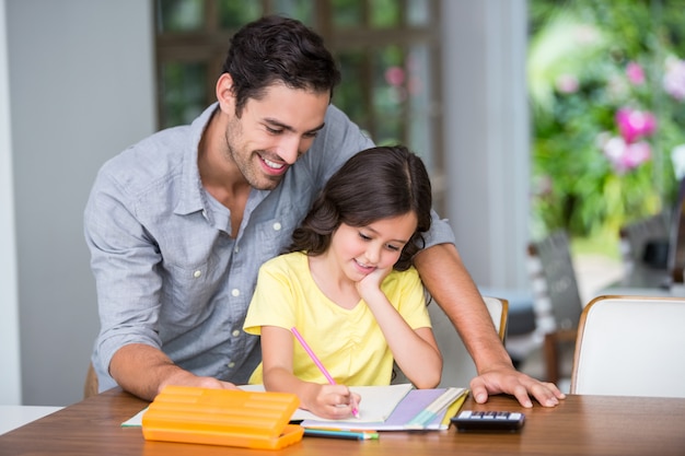 Pai sorridente, ajudando a filha com a lição de casa