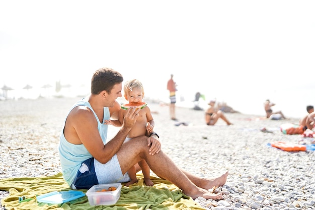 Pai sorridente alimentando menina com fatia de melancia na praia