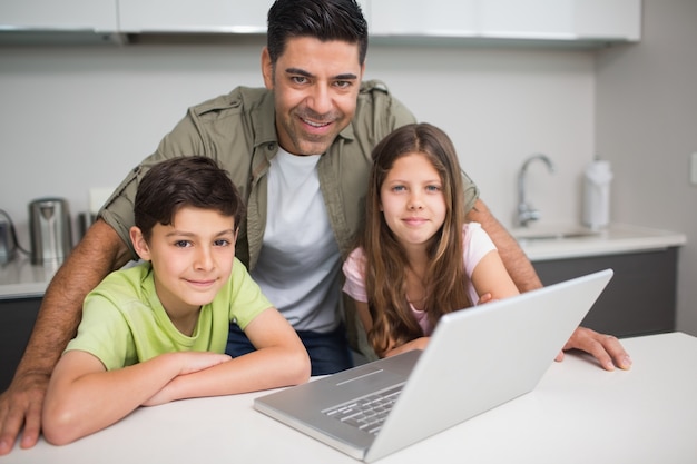 Pai sorridente com crianças usando laptop na cozinha