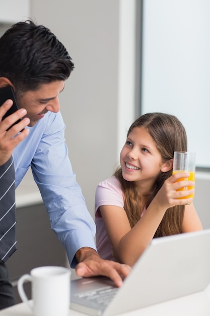 Pai sorridente com filha usando laptop na cozinha